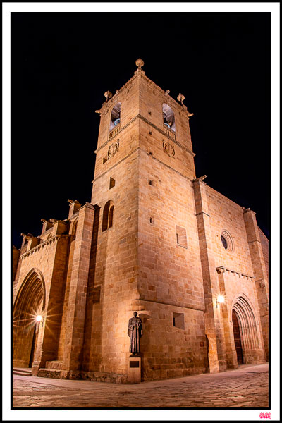 Fachada iluminada de la Concatedral de Santa María en Cáceres de noche, con la estatua de San Pedro de Alcántara en primer plano.